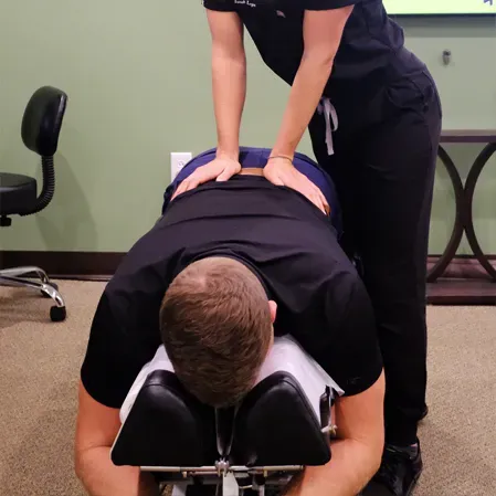 Person lying face down on a chiropractic table while another applies pressure with both hands to the lower back.