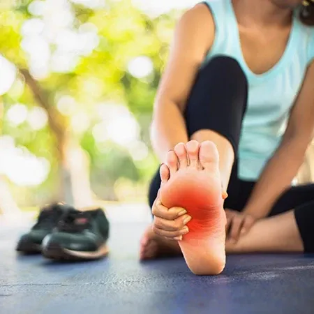 Person seated on ground holding the sole of one foot with one hand, with a red highlighted area on the bottom.